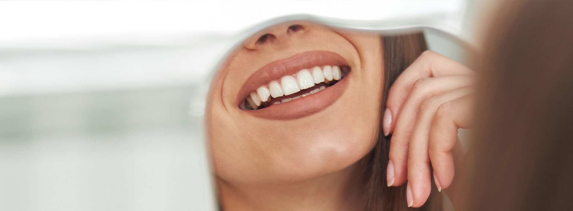 The image is a photograph of a woman with light skin, smiling at the camera. She appears to be in her late twenties or early thirties and has long hair. Her eyes are looking directly at the camera, and she is holding up her index finger near her mouth as if she s making a point or emphasizing something. The background is plain and light-colored, which suggests that this could be a stock photo used for various purposes such as advertising, personal branding, or lifestyle content.