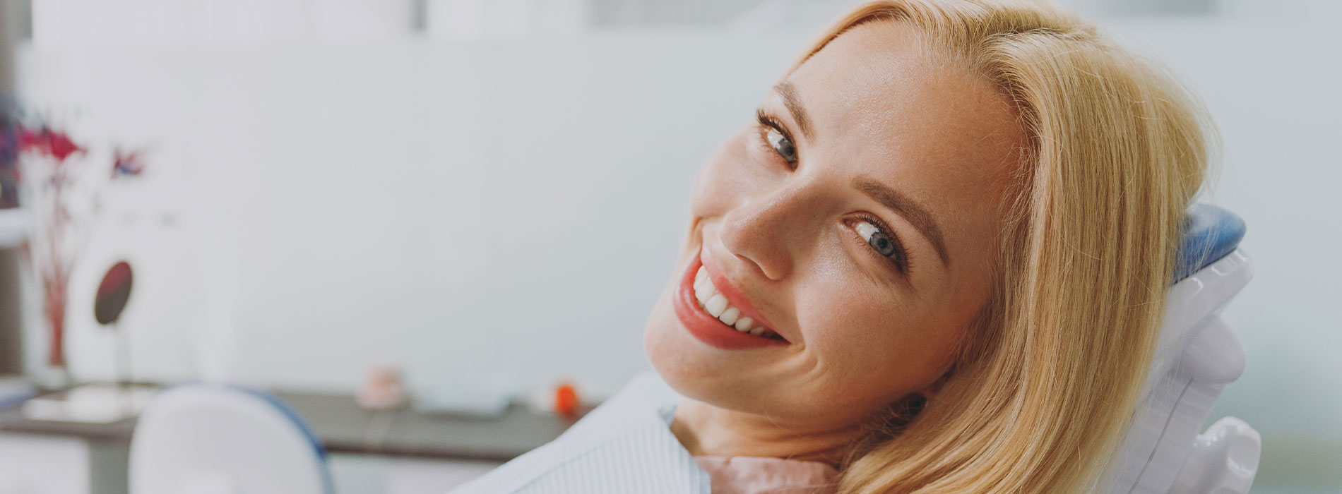 A person is seated in a dental chair, receiving care from a dental professional who stands behind them.